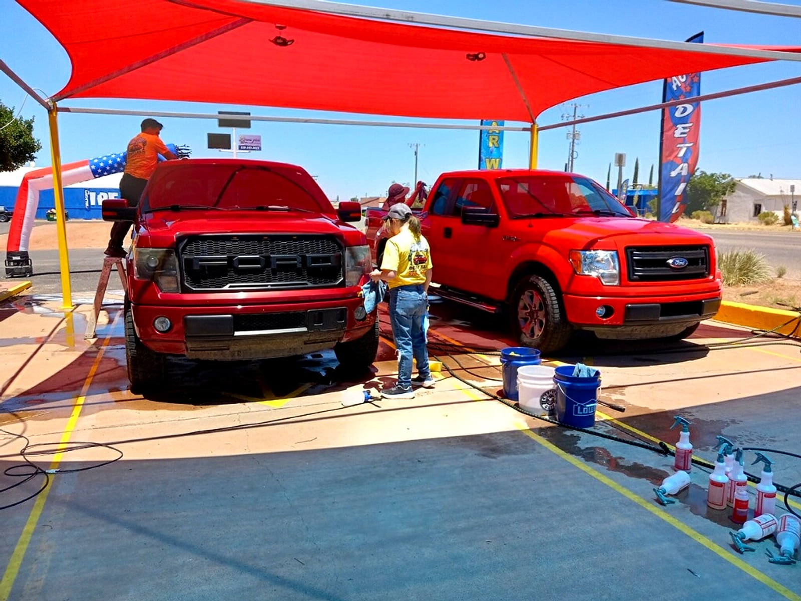 Two red pickup trucks being washed under the red shade canopy